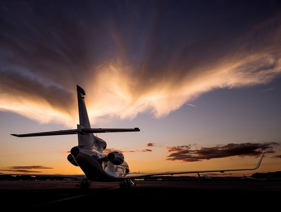 A parked Dassault Falcon jet facing a moody sunset sky