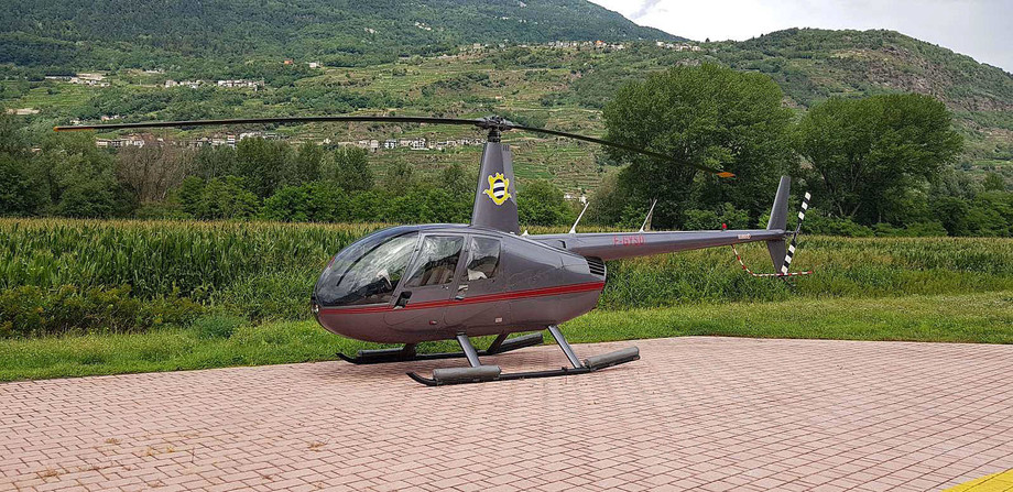 2003 robinson r44 raven II parked on brick paving with a crop field behind rising to a hillside in the distance with buildings in view 