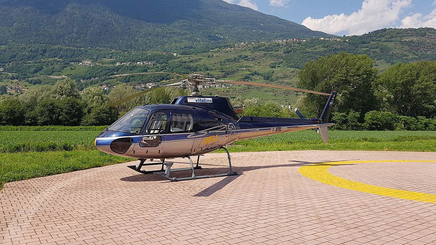 1997 eurocopter as350ba parked on paved helipad with yellow paint markings green grass, fields,trees and hillside in distance 