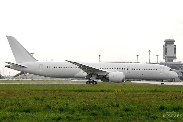 2015 boeing 787-9 on airfield with grass verges communications tower in background grey sky